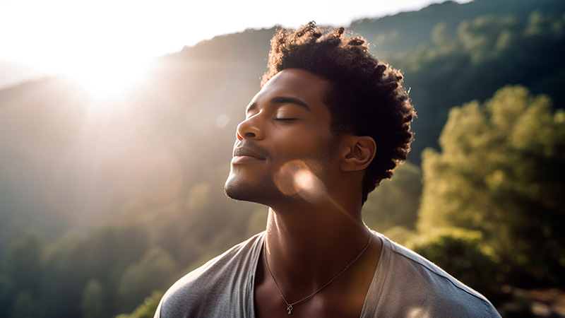 Closeup of young black male with eyes closed meditating outdoors.