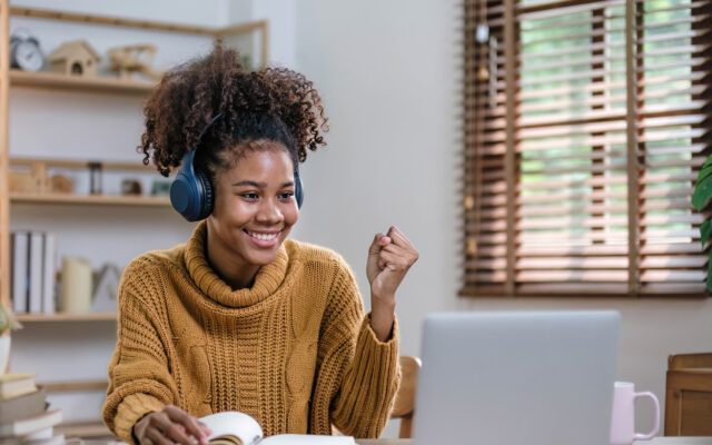 Female student with headphones smiles at laptop in online meeting.