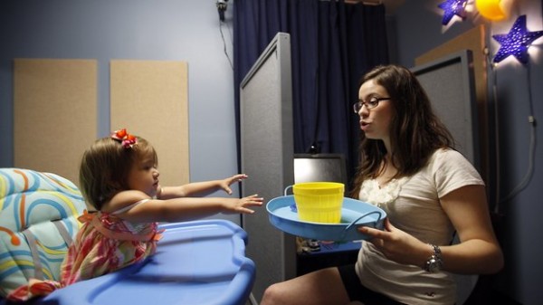 picture of young girl in hospital bed reaching for a bowl in the hands of a doctoral student