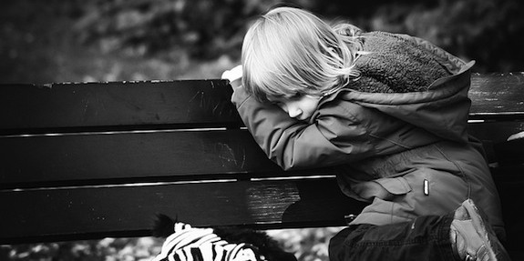 Child on outside bench head down looking depressed