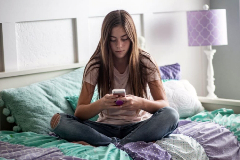 Young female sitting on bed using cell phone.