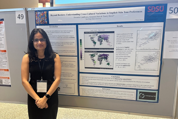 Student standing next to her research presentation poster at a conference