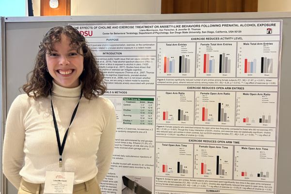 Student standing next to her research presentation poster at a conference