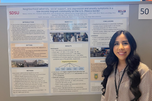 Student standing next to her research presentation poster at a conference
