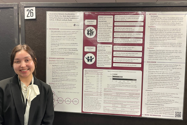 Student standing next to her research presentation poster at a conference