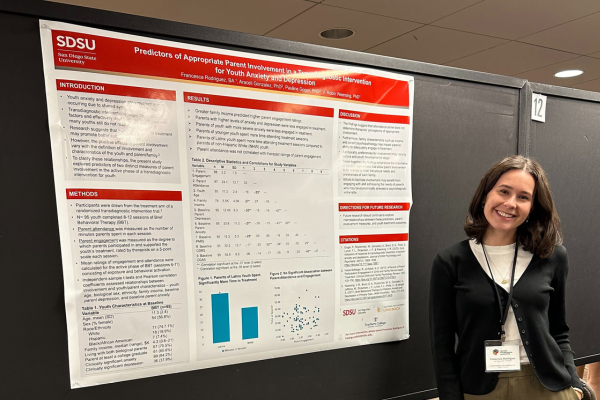 Female student standing next to her research presentation poster at a conference