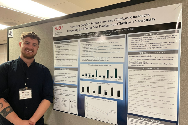 Student standing next to his research presentation poster at a conference