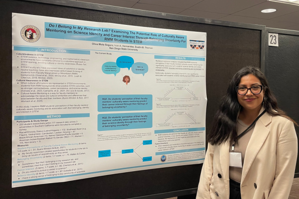 Student standing next to her research presentation poster at a conference