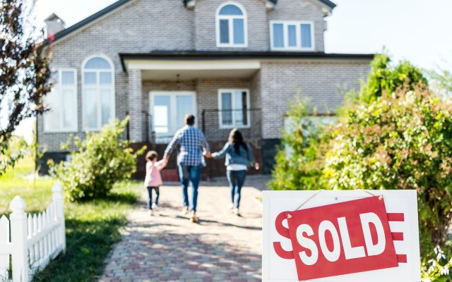 soft focus child, father, and mother holding hands walking away from viewer towards a house with SOLD sign in foreground.